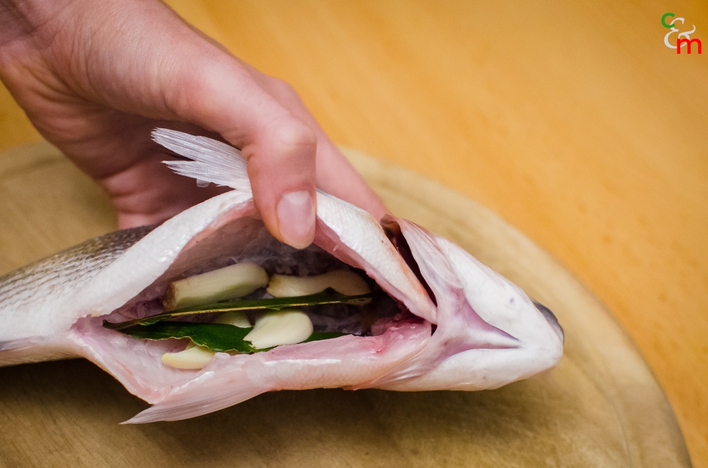 Cospargete con poco sale il ventre del pesce e inseritevi una foglia d&#039;alloro spezzata e metà aglio tagliato a fettine